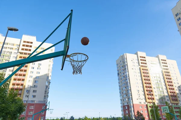 Ein Basketballkorb und ein Schild für Streetbasketball vor dem Hintergrund moderner Wohnhäuser. Bewegung an der frischen Luft mit dem Ball. Basketball-Training. — Stockfoto