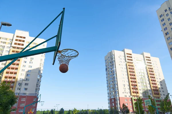 A basketball basket and a shield for street basketball against the background of modern residential buildings. Exercise in the fresh air with the ball. Basketball training.