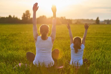 Bir anne ve çocuğu temiz havada yoga yapıyor. Sağlıklı yaşam tarzı kavramı. Açık hava eğlencesi. Meditasyon ve yoga dersleri