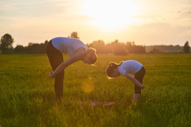 Bir anne ve çocuğu temiz havada yoga yapıyor. Sağlıklı yaşam tarzı kavramı. Açık hava eğlencesi. Meditasyon ve yoga dersleri