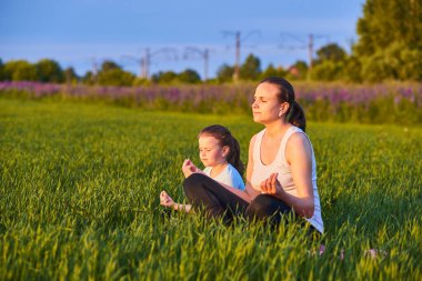 Bir anne ve çocuğu temiz havada yoga yapıyor. Sağlıklı yaşam tarzı kavramı. Açık hava eğlencesi. Meditasyon ve yoga dersleri