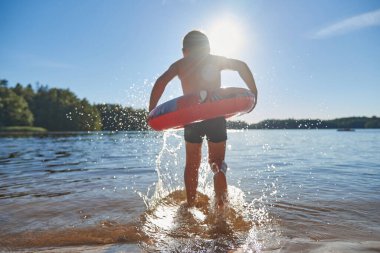 Çemberli bir çocuk gölde yıkanır. Çocuk yüzmeye hazır bir şekilde suya koşar. Çocuklarla açık hava eğlencesi kavramı