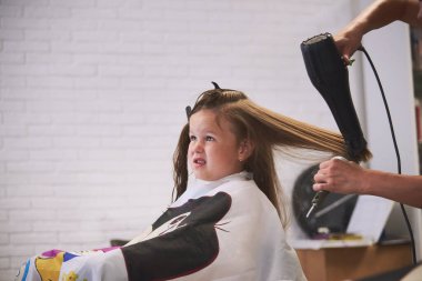 Berber dükkanında küçük bir kız. Çocukların saç kesimi, saç kurutma, tarama ve şekillendirme. Çocuk mutlu ve halinden memnun. Berber steyşın.