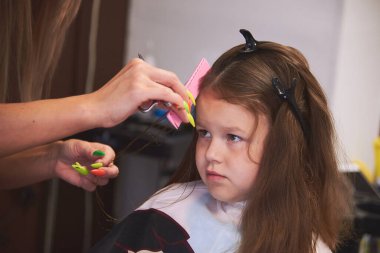 Berber dükkanında küçük bir kız. Çocukların saç kesimi, saç kurutma, tarama ve şekillendirme. Çocuk mutlu ve halinden memnun. Berber steyşın.