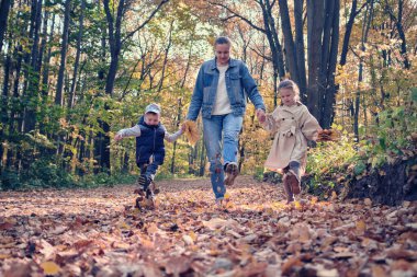 Aile sonbahar ormanında yürür. Anne ve iki çocuğu düşmüş yapraklar üzerinde koşuyorlar..