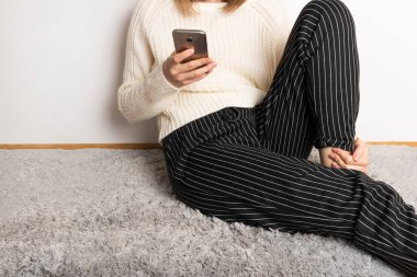 Kadın pofuduk halıya oturur ve telefona bakar..