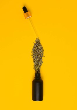 Kozmetik siyah, buzlu cam damlatıcısı şişesi sarı arka planda. Lavanta çiçekleri küçük damlalar gibi şişeye saçılırlar. Deri bakımı konsepti. düz yat.