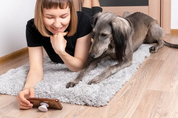 一个带着狗的年轻女人在家里躺在柔软的地毯上 与亲戚通电话 — 图库照片