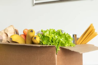 İzole bir arka planda yiyecek dolu bir kutu. Kutuda sebze, meyve, muz, havuç, yumurta, taze salata, spagetti, konserve yiyecekler var. Bağış kavramı, ev yemeği.