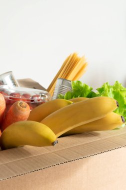 İzole bir arka planda yiyecek dolu bir kutu. Kutuda sebze, meyve, muz, havuç, yumurta, taze salata, spagetti, konserve yiyecekler var. Bağış kavramı, ev yemeği.