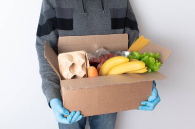 Mavi koruyucu eldivenli bir kurye bir kutu yiyecek getiriyor. Ev teslimatı kavramı