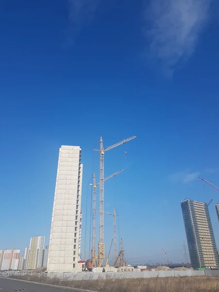 Açık mavi gökyüzüne karşı yeni bir konut inşaatı. Evin yanında yüksek inşaat vinçleri var..