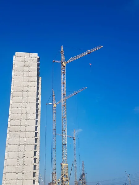 Açık mavi gökyüzüne karşı yeni bir konut inşaatı. Evin yanında yüksek inşaat vinçleri var..