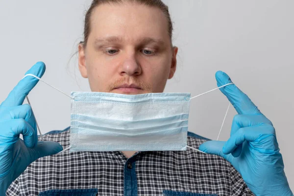 Guy puts on respiratory mask. Attractive man puts on face mask and looks at camera. Cold, flu, virus, tonsillitis, acute respiratory disease, quarantine, epidemic concept. Close-up.