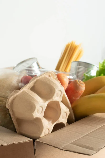 Box filled with food on an isolated background. In the box are vegetables, fruits, bananas, carrots, eggs, fresh salad, spaghetti, canned foods. Concept of donation, home delivery food