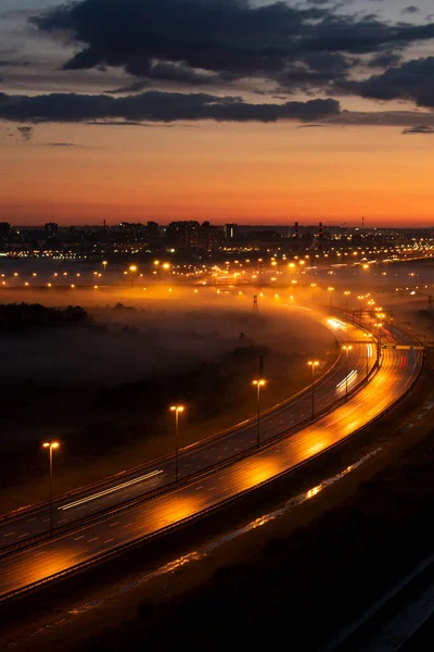 Sisin içinde gece yolu. Farlardan gelen parlak ışık uzun süre maruz kaldıktan sonra yol boyunca uzanıyor.