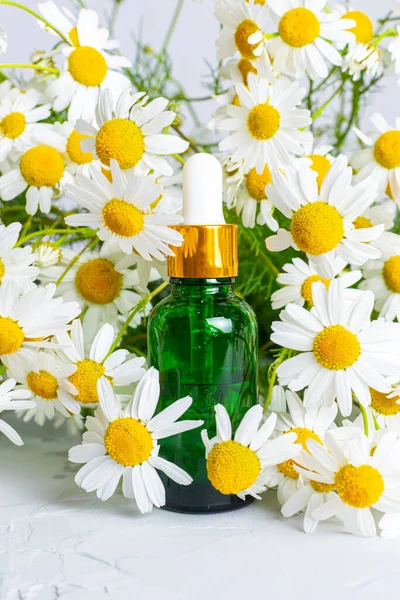Kokulu papatyaların arka planına karşı cam damlatan yeşil bir şişe. Doğal kozmetik ürünleri ve cilt bakımı. Aroma esaslı yağ