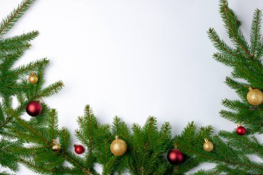 Beyaz arka planda kırmızı ve altın renkli Noel oyuncakları ile süslenmiş köknar dalları. Metin için yer