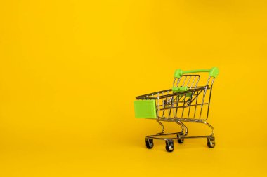 Sarı arka planda süpermarketten gelen küçük boş metal tramvay. Yatay fotoğraf. Ticaret konsepti. Boşluğu kopyala.