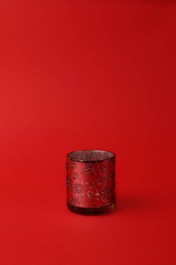 Kırmızı zemin üzerinde kar taneleri süsü olan cam şamdan. Dikey fotoğraf. Uzayı kopyala Noel konsepti. Minimalizm.