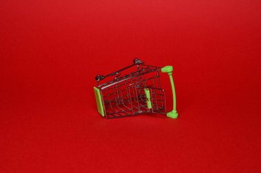 Bir süpermarketten gelen küçük boş bir metal tramvay kırmızı arka planda yatar. Yatay fotoğraf. ticaret kavramı.