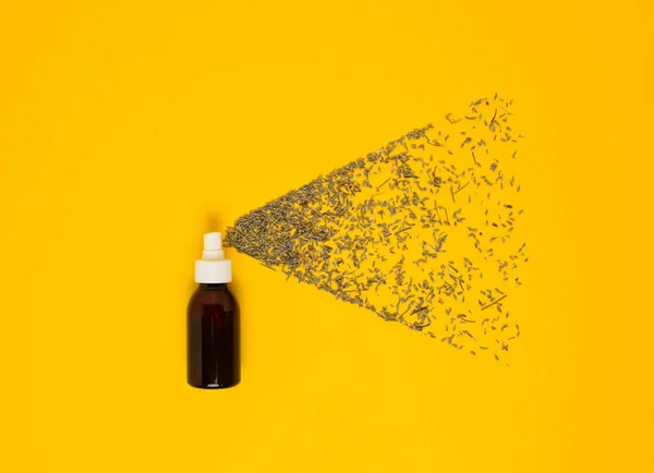 Transparent cosmetic amber glass spray bottle on a yellow background. Lavender flowers scatter like small droplets from a spray. flat lay.