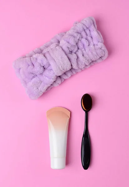 Cosmetics and accessories on a pink background. Black makeup brush, foundation and purple headband on a pink background. flat lay