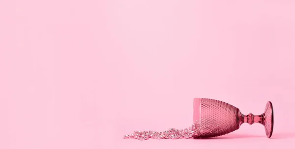 a pink glass and beads lie against a pastel pink background. Minimalism. Copy space.