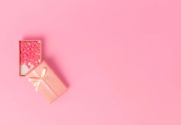 Pembe arka planda, çerçevenin ortasında bir fiyonk olan pembe bir hediye. Yukarıdan bak. Küçük şeker kalpler hediye kutusunda yatıyor. Boşluğu kopyala