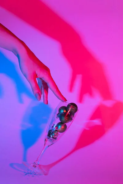 Dişi el, yılbaşı toplarıyla dolu bir bardak şampanya tutuyor. Moda neon renkli fotoğraf. yeni yıl konsepti