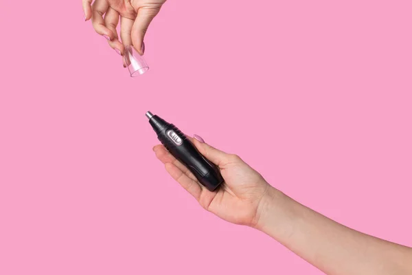 Kadın eli, erkeğin elektrikli maşasını nazikçe tutar. Pastel pembe arka planda minimalizm