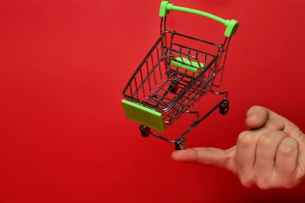 Bir adamın el bakiyesinde, küçük boş bir metal süpermarket tramvayı. Nesne kırmızı arka planda. Yatay fotoğraf. ticaret kavramı.