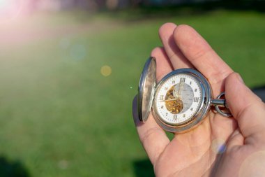 Yeşil çimenlerin üzerine erkek eli takılmış klasik cep saati. Steampunk saati. Güneşli bir yaz günü. Saat mekanizması kısmen görünür..