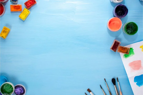 Sanat malzemeleri: suluboya, akrilik, fırçalar ve mavi arka planda palet. Düz yerde, üst tarafta. Sanatçının minimalist masaüstü. Çizim için hazırlama.