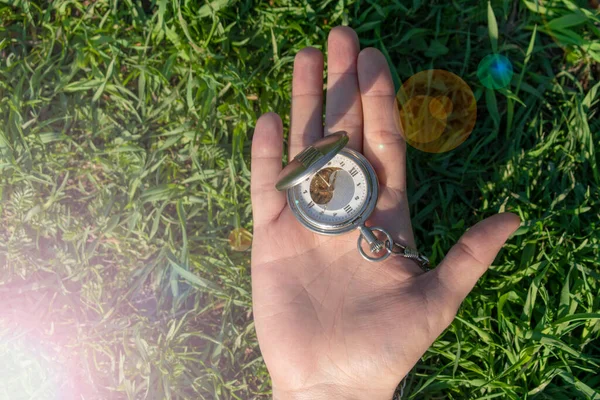 Yeşil çimenlerin üzerine erkek eli takılmış klasik cep saati. Steampunk saati. Güneşli bir yaz günü. Saat mekanizması kısmen görünür..