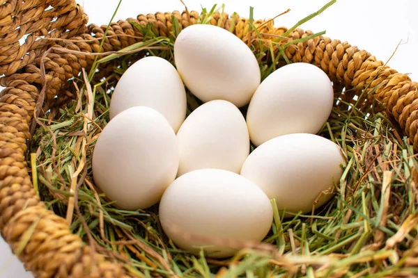 Beyaz arka planda saman üzerinde hasır bir sepetteki beyaz yumurtalar
