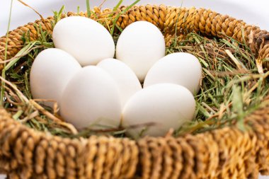 Beyaz arka planda saman üzerinde hasır bir sepetteki beyaz yumurtalar