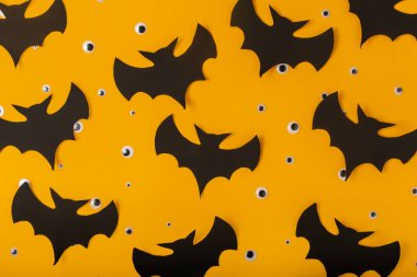 Cadılar Bayramı arkaplanı sarı renklidir. Plastik gözler ve yarasa siluetleri serpilmiştir.