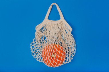 Çerçevenin ortasında yeniden kullanılabilir bir sicim torbasının içindeki turuncu bir balkabağı parlak mavi bir arka plana karşı. Düz yatış minimumda