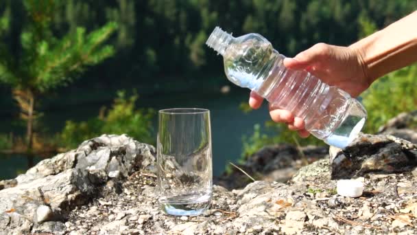 男は、山間部のガラスにボトルからきれいな水を注ぐ。健康とエコロジーのテーマ。スローモーション — ストック動画