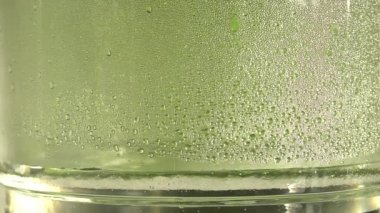 Yeşil zemin üzerine bir cam kavanoz içinde saf su ya da alkol damla damla. Damıtma süreci veya alkol üretimi. Yakın çekim Hd