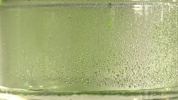 Gotas de agua pura o alcohol gotean dentro de un frasco de vidrio, sobre fondo verde. El proceso de destilación o la producción de alcohol. Primer plano — Vídeo de stock