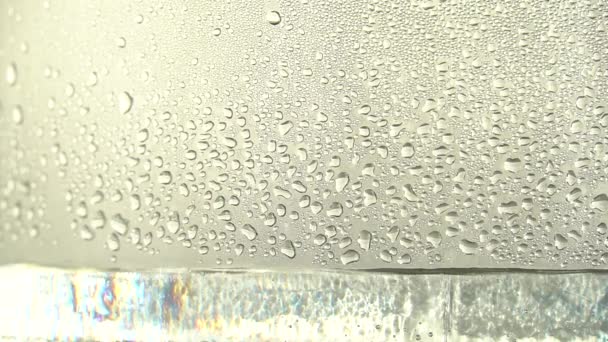 Капли чистой воды или спирта капают в стеклянную банку, на серебряном фоне. Процесс дистилляции или производство алкоголя. Крупный план — стоковое видео