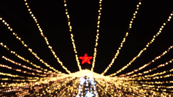 屋外の暗い背景にボケ効果で赤い星とクリスマスツリー。明るいボケで多くのちらつきガーランドとシルエットクリスマスツリー。メリークリスマスとハッピーニューイヤーのコンセプト。4K — ストック動画