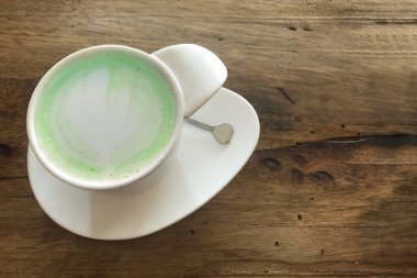 koyu ahşap masa arka plan üzerinde sıcak japnese yeşil çay matcha süt bardağı üstüne kalp sanat şekli tasarım.