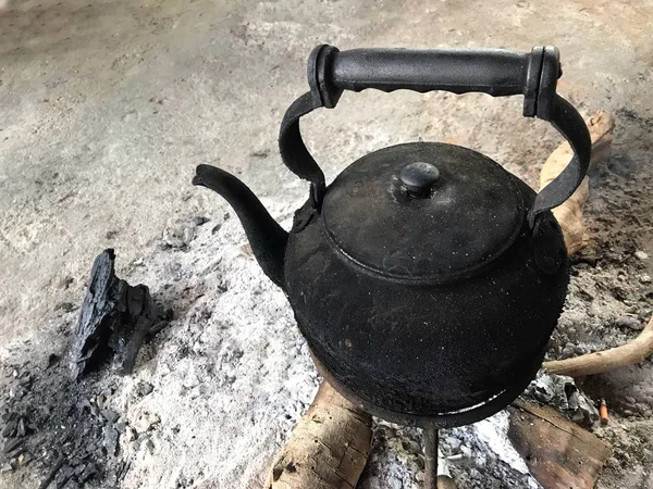 burned Thai vintage black hot teapot on fire charcoals wood.