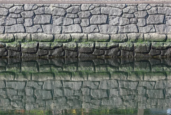 a natural stone wall with reflection on water surface near river side.