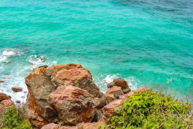 Güneşli bir günde adada dalgalı dalgalı deniz olan doğal taş plajı..