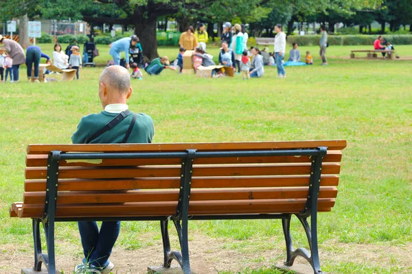 2017 Ekim 06. Tokyo Japonya. Bankta oturan yaşlı bir adam parktaki diğer insanlara bakıyor..