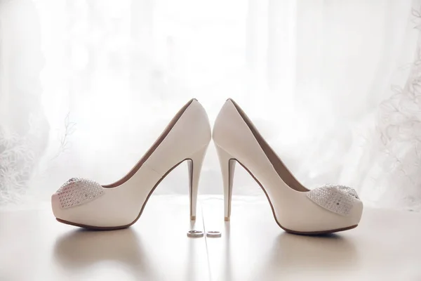 Wedding bridal white shoes with crystals, high heels and wedding rings.